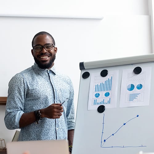 A young confident man explaining some charts which are pinned on the whiteboard