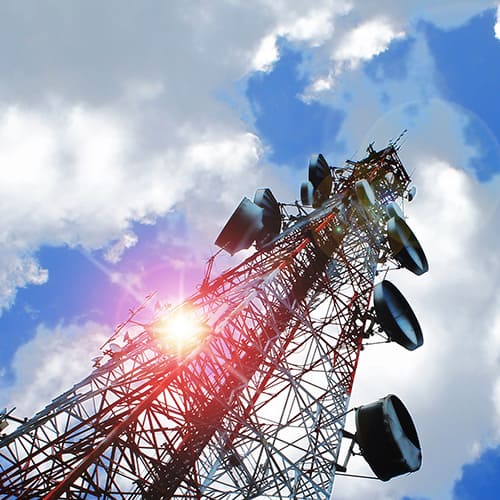 A telecom tower with a sun shining bright in the sky