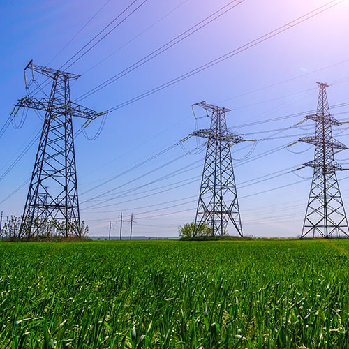 Electrical tower in a green agricultural land with a sun shining bring in the blue sky